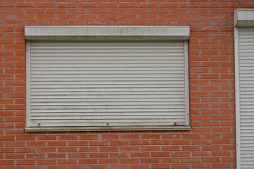 one big window close with white rolls on a red brick wall on the building on the street