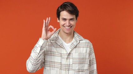Smiling cheerful fun young brunette man 20s years old wears white shirt showing okay ok zero fingers gesture isolated on plain orange wall background studio portrait. People emotions lifestyle concept