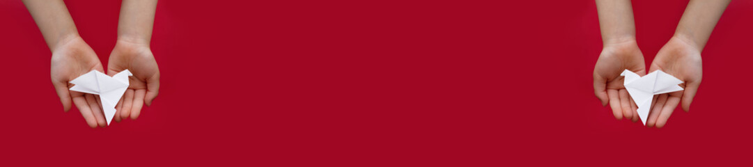 banner two white paper origami pigeon in children's hands on red background
