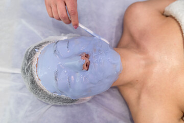 Beautician procedures - dermatolog applying face mask to young woman