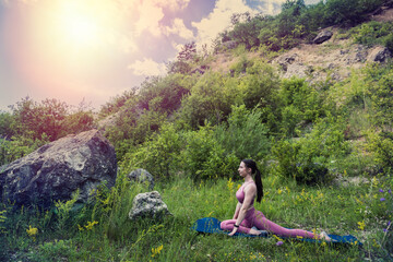  young girl with a beautiful figure in sportswear stretches beautifully on the green grass.