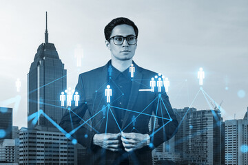 Handsome eastern HR director at international company thinking about efficient strategy to recruit highly qualified specialists. Social media and marketing hologram icons over Kuala Lumpur background