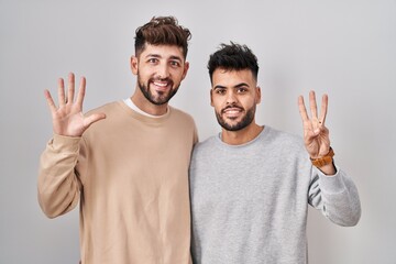 Young homosexual couple standing over white background showing and pointing up with fingers number eight while smiling confident and happy.