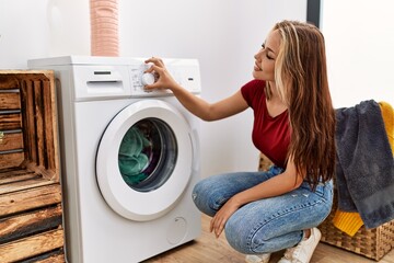 Young caucasian girl smiling happy cleaning clothes using whasing machine at home.