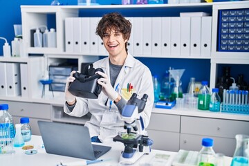 Young hispanic man scientist holding virtual reality glasses at laboratory