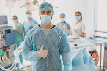 Portrait of surgeon standing in operating room and showing thumb up, ready to work on patient