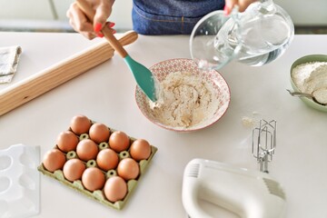 Young blonde woman pouring water on bowl at kitchen