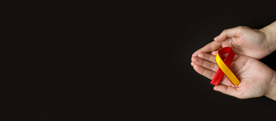 World hepatitis day. Adult hands holding red yellow ribbon on black background. Awareness of prevention and treatment viral hepatitis. Liver cancer. World cancer day. copy space. banner