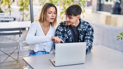 Young man and woman couple using laptop sitting on table at coffee shop terrace