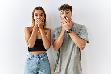 Young beautiful couple standing together over isolated background shocked covering mouth with hands for mistake. secret concept.