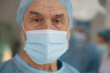 Close up of senior surgeon in mask standing in operating room, ready to work on patient
