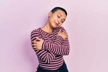 Obraz premium Beautiful hispanic woman with short hair wearing casual striped sweater hugging oneself happy and positive, smiling confident. self love and self care