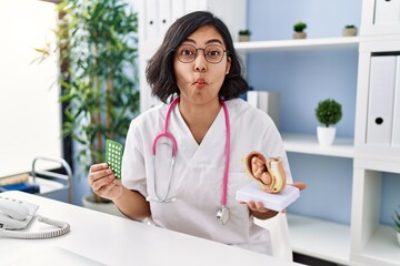 Young hispanic doctor woman holding anatomical model of uterus with fetus and birth control pills...