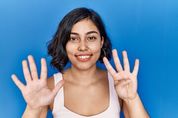 Young hispanic woman standing over blue background showing and pointing up with fingers number nine...