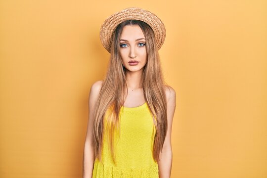 Young blonde girl wearing summer hat relaxed with serious expression on face. simple and natural looking at the camera.