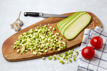 Courgette zucchini diced sliced on a wooden cutting board, tomatoes, garlic on a concrete light table