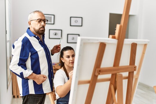 Senior painting teacher man teaching art to young woman painting on canvas at art studio