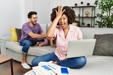 Mother of interracial family working using computer laptop at home surprised with hand on head for mistake, remember error. forgot, bad memory concept.