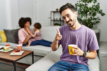 Hispanic father of interracial family drinking a cup coffee pointing fingers to camera with happy and funny face. good energy and vibes.