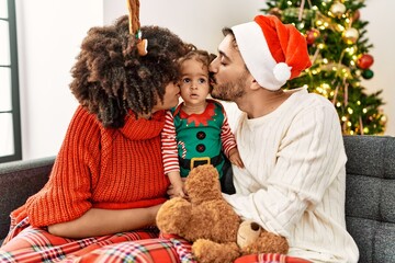 Couple and daughter kissing child sitting by christmas tree at home