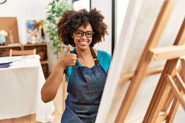 Beautiful african american woman with afro hair painting canvas at art studio smiling happy and positive, thumb up doing excellent and approval sign