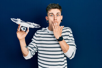 Young caucasian boy with ears dilation holding drone covering mouth with hand, shocked and afraid...