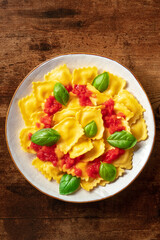 Ravioli with tomato sauce and fresh basil on a plate. Healthy Italian meal, shot from above on a dark rustic wooden background