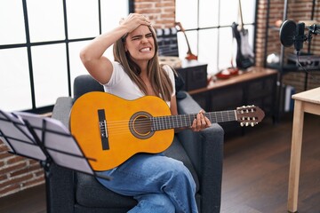 Young beautiful woman playing classic guitar at music studio stressed and frustrated with hand on...