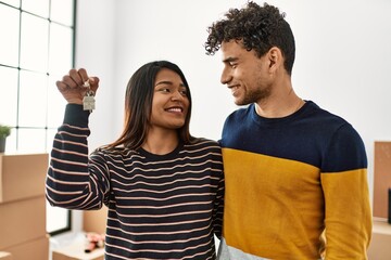 Young latin couple smiling happy and hugging holding key of new home.