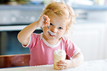 Adorable baby girl eating from spoon sweet ice cream in waffle cone. food, child, feeding and...