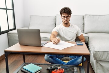 Hispanic man doing papers at home skeptic and nervous, frowning upset because of problem. negative person.