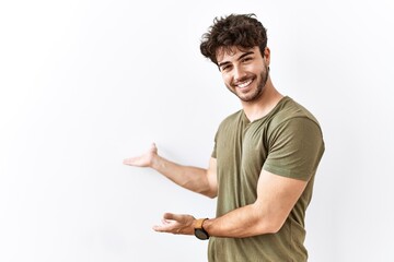 Hispanic man standing over isolated white background inviting to enter smiling natural with open...
