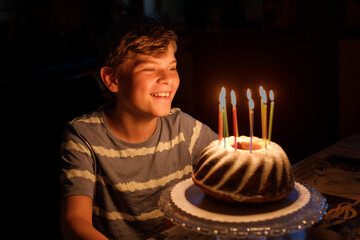 Happy blond little kid boy celebrating his birthday. Child blowing candles on homemade baked cake,...