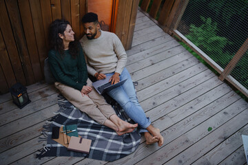 Top view of happy couple with laptop resting outdoors in a tree house, weekend away and remote office concept.