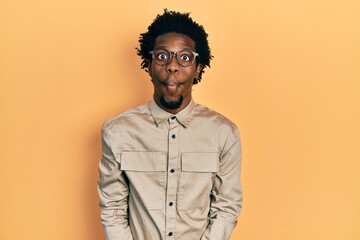 Obraz premium Young african american man wearing casual clothes and glasses making fish face with lips, crazy and comical gesture. funny expression.