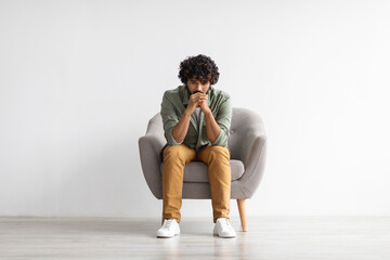 Depressed indian guy sitting in armchair over white