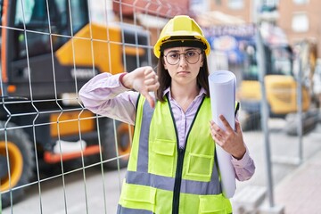 Hispanic girl wearing architect hardhat at construction site with angry face, negative sign showing...