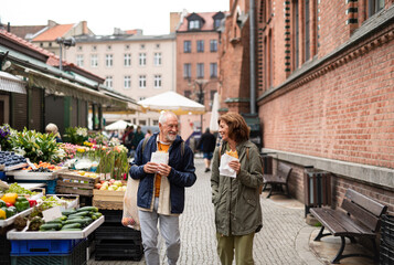 Fototapeta na wymiar Happy senior couple tourists with snack in town on outdoor market.