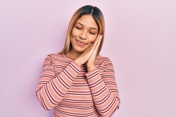 Fototapeta premium Beautiful hispanic woman wearing casual striped sweater sleeping tired dreaming and posing with hands together while smiling with closed eyes.