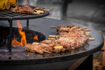 Selective focus of preparing of picnic meal made of roasted shish-kebab or skewered beef or pork meat on outdoor barbecue grill with fire flame and smoke at outside kitchen of street food restaurant