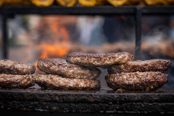 Group of patties flattened round, serving of minced ground beef meat being roasted on outdoor barbeque grill with orange flame at outdoor kitchen of street food restaurant used for burgers cooking