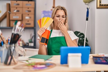 Young caucasian woman doing video call showing color palette covering mouth with hand, shocked and...