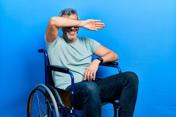 Obraz premium Handsome middle age man with grey hair sitting on wheelchair covering eyes with arm smiling cheerful and funny. blind concept.