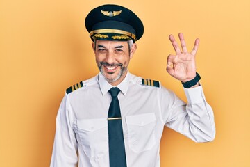 Handsome middle age man with grey hair wearing airplane pilot uniform smiling positive doing ok...