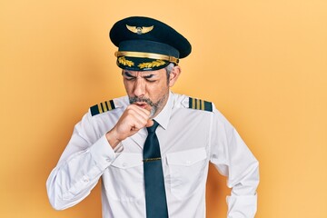 Handsome middle age man with grey hair wearing airplane pilot uniform feeling unwell and coughing...