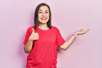 Middle age hispanic woman wearing casual clothes showing palm hand and doing ok gesture with thumbs up, smiling happy and cheerful