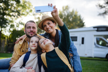 Happy young family with two children taking selfie with caravan at background outdoors. - obrazy, fototapety, plakaty