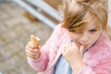 Little preschool girl eating ice cream in waffle cone on sunny summer day. Happy toddler child eat icecream dessert. Sweet food on hot warm summertime days. Bright light, colorful ice-cream
