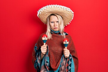 Beautiful caucasian blonde woman wearing festive mexican poncho and maracas skeptic and nervous, frowning upset because of problem. negative person.