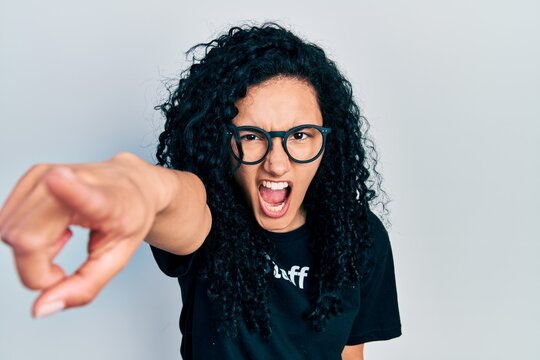 Young hispanic woman with curly hair wearing staff t shirt pointing displeased and frustrated to the camera, angry and furious with you